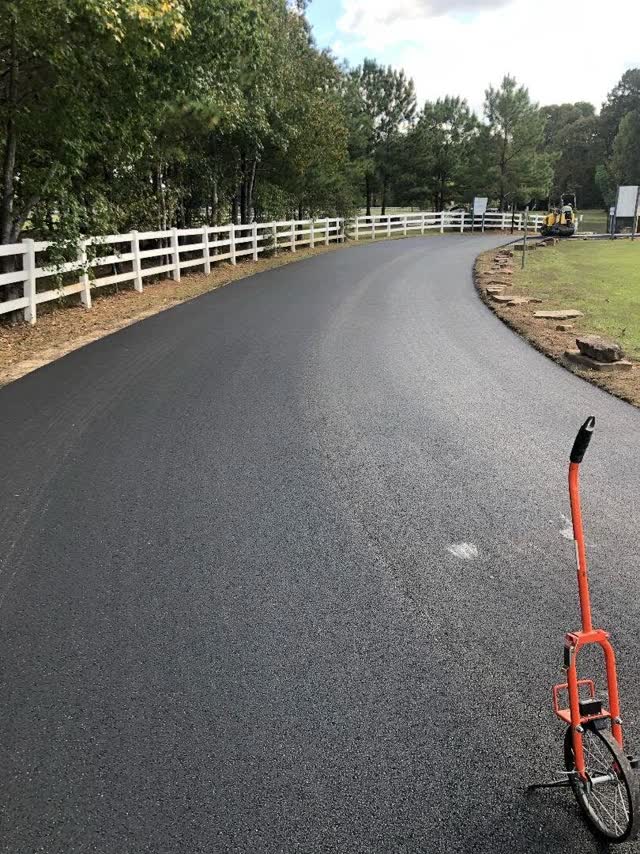 Curved jet-black driveway along a white three-rail fence