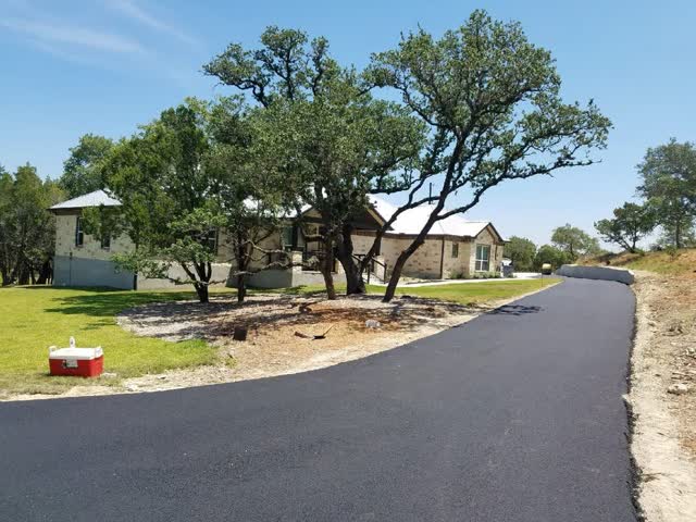 Fresh asphalt driveway curving past a stone home