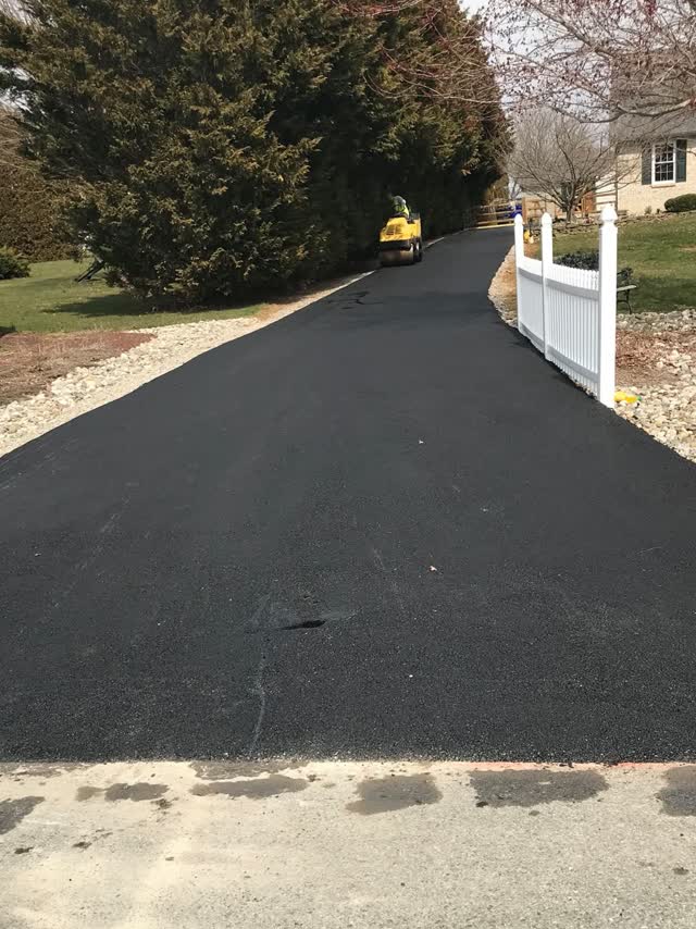 Fresh blacktop driveway beside a white picket fence